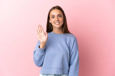 Soyutlanmış pembe arka planda genç bir kadın. Mutlu bir ifadeyle selamlıyor.