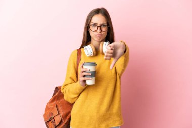 Soyutlanmış pembe arka planda genç bir bayan, olumsuz bir ifadeyle baş parmağını aşağı gösteriyor.