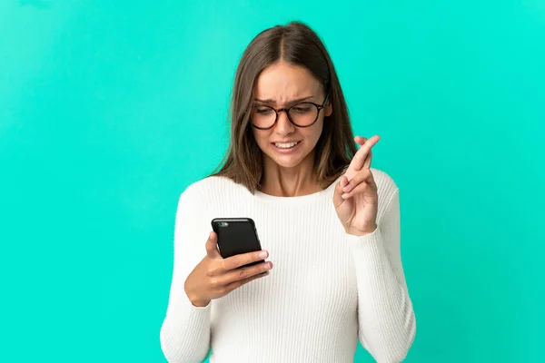 Junge Frau Über Einsamen Blauen Hintergrund Mit Handy Mit Daumendrücken — Stockfoto