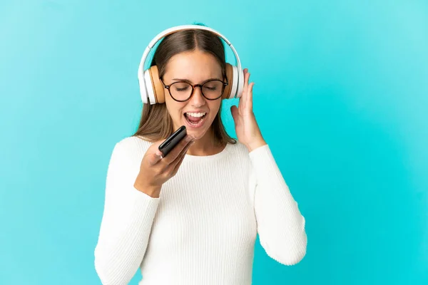 Mujer Joven Sobre Fondo Azul Aislado Escuchando Música Con Móvil — Foto de Stock