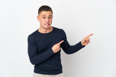 Beyaz arka planda izole edilmiş genç beyaz adam korkmuş ve kenarı işaret ediyor.