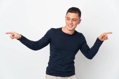 Beyaz arka planda izole edilmiş genç beyaz adam parmak uçlarını işaret ediyor ve mutlu.