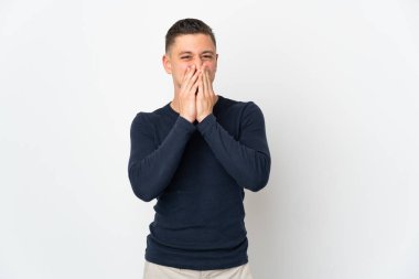 Beyaz arka planda izole edilmiş genç beyaz bir adam mutlu ve gülümseyen elleriyle ağzını kapatıyor.