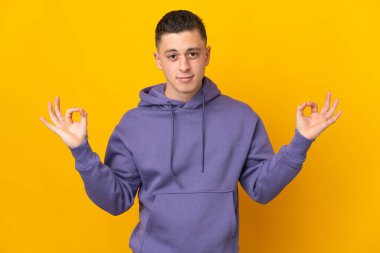 Zen pozisyonunda sarı arka planda izole edilmiş genç beyaz adam.