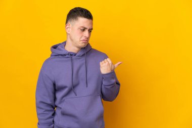 Sarı arka planda izole edilmiş genç beyaz adam mutsuzdu ve yan tarafı gösteriyordu.