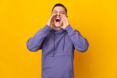 Genç beyaz adam sarı arka planda izole edilmiş bağırıyor ve bir şey duyuruyor.