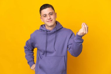 Sarı arka planda izole edilmiş genç beyaz adam İtalyan jestleri yapıyor.