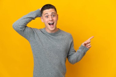 Sarı arka planda izole edilmiş genç beyaz adam şaşırdı ve parmağını yana çevirdi.