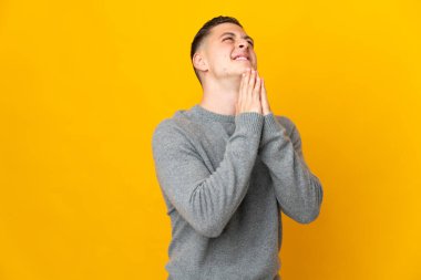 Sarı arka planda izole edilmiş genç beyaz adam avuç içlerini bir arada tutuyor. İnsan bir şey ister.