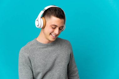 Genç beyaz adam mavi arka planda izole edilmiş müzik dinliyor.