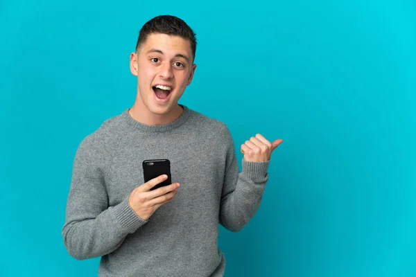 Joven Hombre Caucásico Aislado Sobre Fondo Azul Usando Teléfono Móvil — Foto de Stock