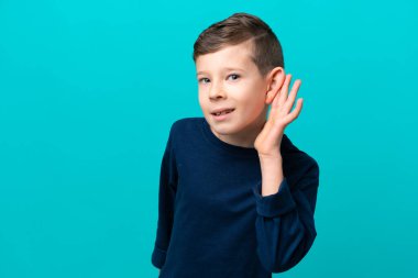 Küçük çocuk mavi arka planda izole edilmiş bir şekilde kulağına elini sürerek bir şeyler dinliyor.