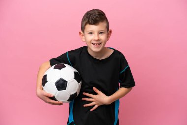 Küçük beyaz futbolcu çocuk pembe arka planda izole edilmiş, çok gülümsüyor.