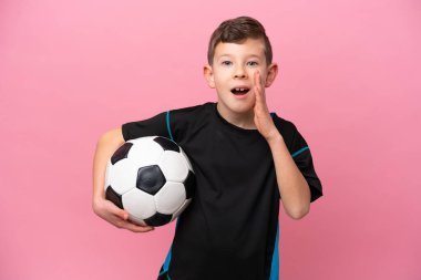 Küçük beyaz futbolcu çocuk pembe arka planda mahsur kalmış, şaşırmış ve şok olmuş bir yüz ifadesi var.