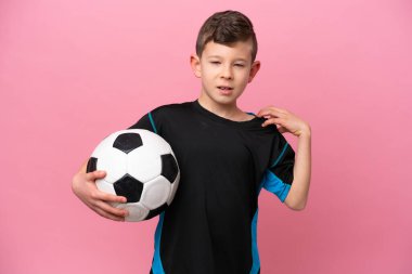 Küçük beyaz futbolcu çocuk, pembe arka planda izole edilmiş. Çabaladığı için omuz ağrısı çekiyor.