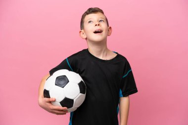 Küçük beyaz futbolcu çocuk pembe arka planda izole edilmiş gülüyor.
