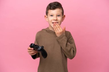 Küçük beyaz bir çocuk pembe arka planda izole edilmiş bir bilgisayar oyunu kontrolörüyle oynuyor.
