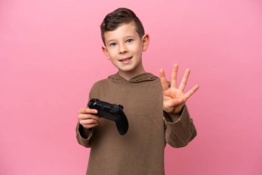 Pembe arka planda izole edilmiş bir bilgisayar oyunu kontrolörüyle oynayan küçük beyaz çocuk mutlu ve parmaklarıyla dört tane sayıyor.