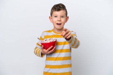 Beyaz arka planda izole edilmiş mısır gevreği kasesi tutan küçük beyaz çocuk şaşırmış ve ön tarafı işaret ediyor.