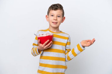 Beyaz arka planda yalıtılmış mısır gevreği kasesi tutan küçük beyaz çocuk, davet etmek için ellerini yana uzatıyor.