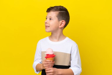 Sarı arka planda izole edilmiş kornet dondurması olan beyaz bir çocuk.