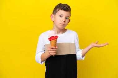 Kornet dondurması olan beyaz bir çocuk sarı arka planda izole edilmiş bir şekilde el kaldırırken şüpheleri var.