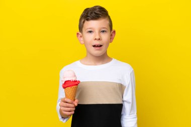 Kornet dondurması olan beyaz bir çocuk sarı arka planda, şaşırmış bir yüz ifadesiyle izole edilmiş.