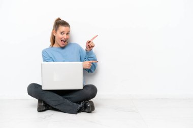 Dizüstü bilgisayarı olan genç bir kadın yerde oturuyor şaşırmış ve işaret ediyor.