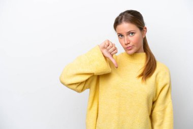 Beyaz arka planda izole edilmiş genç beyaz kadın olumsuz ifade ile baş parmağını aşağı gösteriyor.