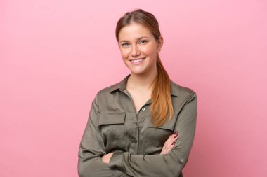 Pembe arka planda izole edilmiş genç beyaz kadın kollarını ön cephede çapraz tutuyor.