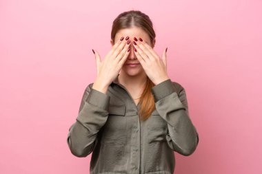 Pembe arka planda izole edilmiş genç beyaz kadın gözlerini elleriyle kapatıyor.