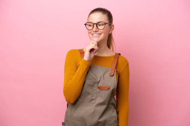 Önlüklü kadın pembe arka planda izole edilmiş, yan tarafa bakıyor ve gülümsüyor.