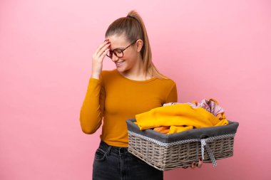 Pembe arka planda izole edilmiş çamaşır sepeti tutan beyaz bir kadın gülüyor.