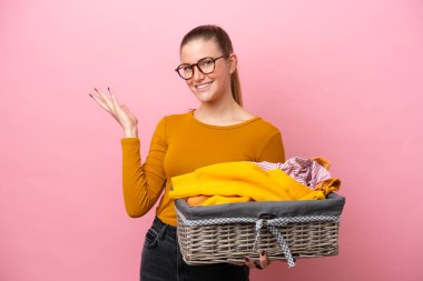 Pembe arka planda izole edilmiş çamaşır sepeti tutan beyaz bir kadın davet edildiği için ellerini yana uzatıyor.