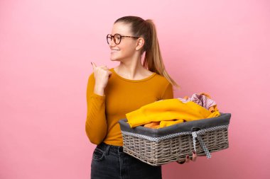 Genç beyaz kadın pembe arka planda izole edilmiş bir çamaşır sepeti tutuyor. Yan tarafı göstererek bir ürün sunuyor.