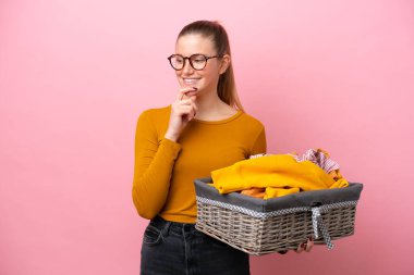 Pembe arka planda izole edilmiş çamaşır sepetini tutan beyaz bir kadın yana bakıyor ve gülümsüyor.
