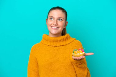 Mavi arka planda yalıtılmış tart tutan beyaz bir kadın gülümserken yukarı bakıyor.