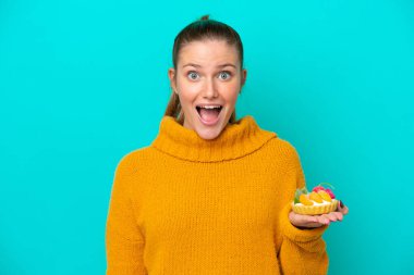 Elinde turta tutan beyaz bir kadın mavi arka planda şaşırmış ve şok olmuş bir yüz ifadesiyle izole edilmiş.