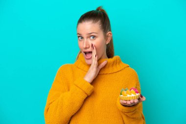 Mavi arka planda izole edilmiş tart tutan beyaz bir kadın bir şeyler fısıldıyor.