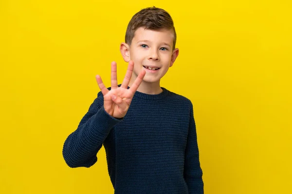 黄色の背景に孤立した小さな白人の少年幸せと指で4を数える — ストック写真