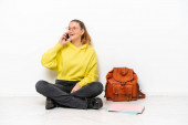 Mladý student běloška žena sedí jeden na podlaze izolované na bílém pozadí vedení konverzace s mobilním telefonem
