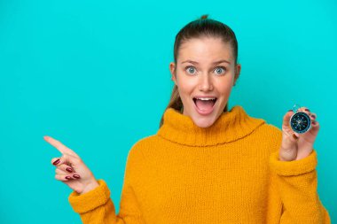 Elinde pusula tutan beyaz bir kadın mavi arka planda izole edilmiş, şaşırmış ve parmağıyla kenarı işaret ediyor.