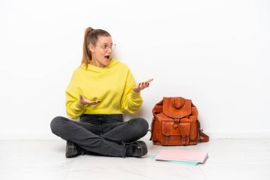 Beyaz arka planda beyaz bir zeminde oturan beyaz yüzlü genç beyaz bir kadın.