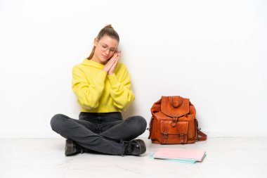 Beyaz arka planda beyaz bir zeminde oturan beyaz tenli genç bir kadın, hareketli bir uyku hareketi yapıyor.