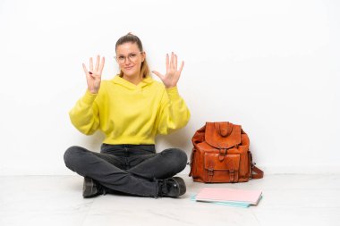 Beyaz arka planda bir katta oturan beyaz tenli genç bir kadın dokuz parmaklı sayıyor.