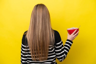 Sarı arka planda izole edilmiş bir kase mısır gevreği tutan beyaz bir kadın.