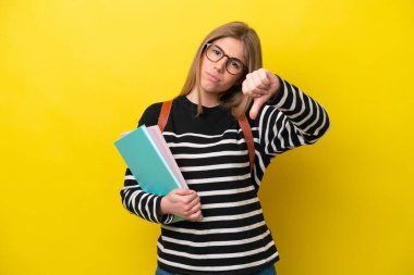 Sarı arka planda izole edilmiş genç bir bayan, olumsuz ifade ile baş parmağını gösteriyor.