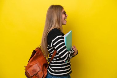 Sarı arka planda izole edilmiş genç bir bayan. Yan pozisyonda gülüyor.