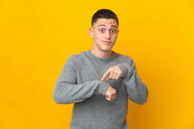 Sarı arka planda izole genç beyaz adam geç kalma jesti yapıyor