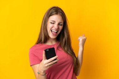 Sarı arka planda cep telefonu kullanan genç bir kadın zaferi kutluyor.